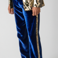 A man wearing blue velvet trousers with gold satin edges and a blue velvet jacket with gold satin edges and cutout elbows with satin edges, the man has a 60cm bone spike protruding from each elbow, his hair is black and slicked back